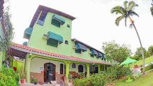 Un edificio de dos pisos con fachada verde, un porche cubierto y una palmera al fondo.