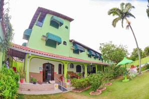 Un edificio de dos pisos con fachada verde, un porche cubierto y una palmera al fondo.