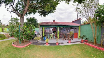 A building with a red-tiled roof, a green awning, and a small outdoor seating area with chairs and tables.