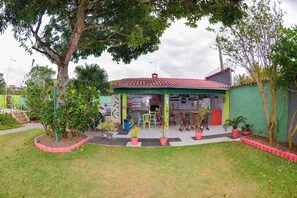 A building with a red-tiled roof, a green awning, and a small outdoor seating area with chairs and tables. - VOA Pousada Dos Jasmins (Serra)