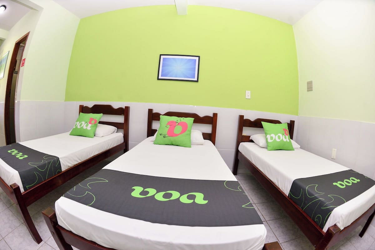 Una habitación de hotel con tres camas individuales, cada una con una colcha verde y blanca y un almohadón con una letra.