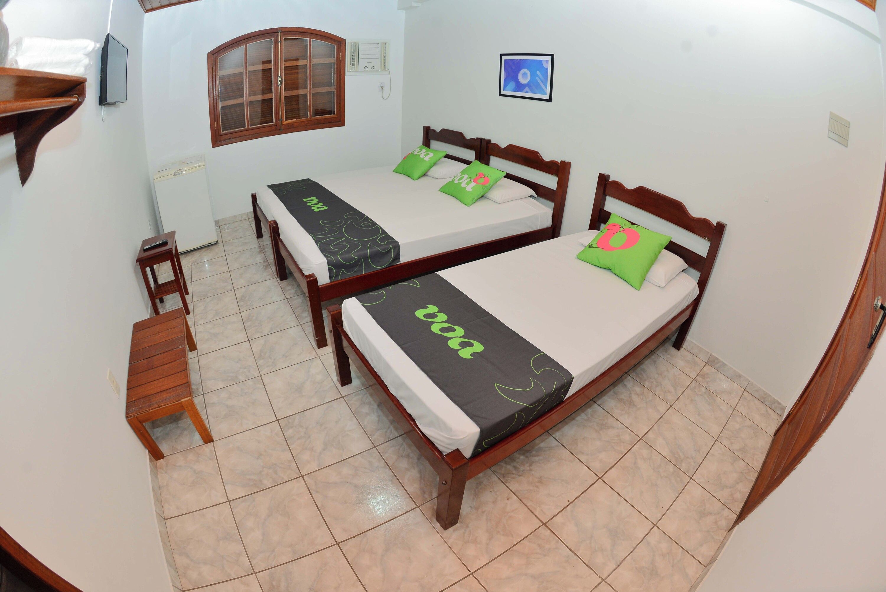 A room with two wooden beds, a small table, a chair, a window, and a wall-mounted TV.