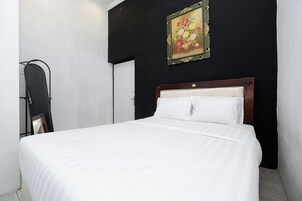 Uma cama com roupa de cama branca, cabeceira de madeira e um quadro de flores na parede.