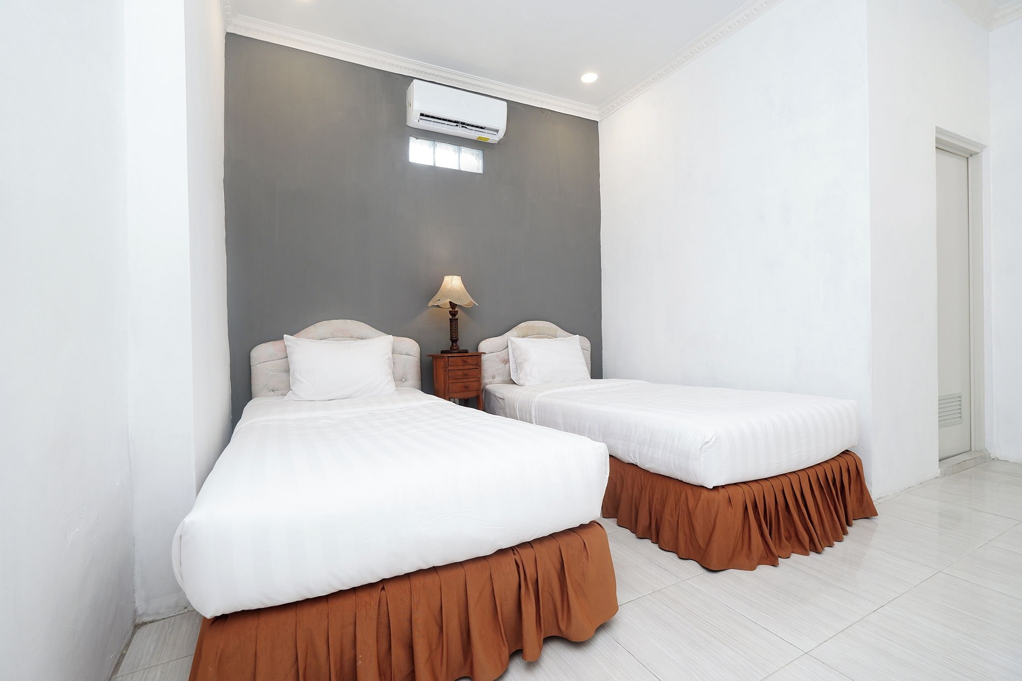 A hotel room with two beds, a nightstand, a lamp, and an air conditioning unit.