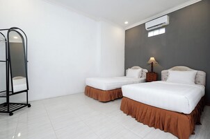 Habitación de hotel con dos camas, una lámpara de pie, un equipo de aire acondicionado y una estantería.
