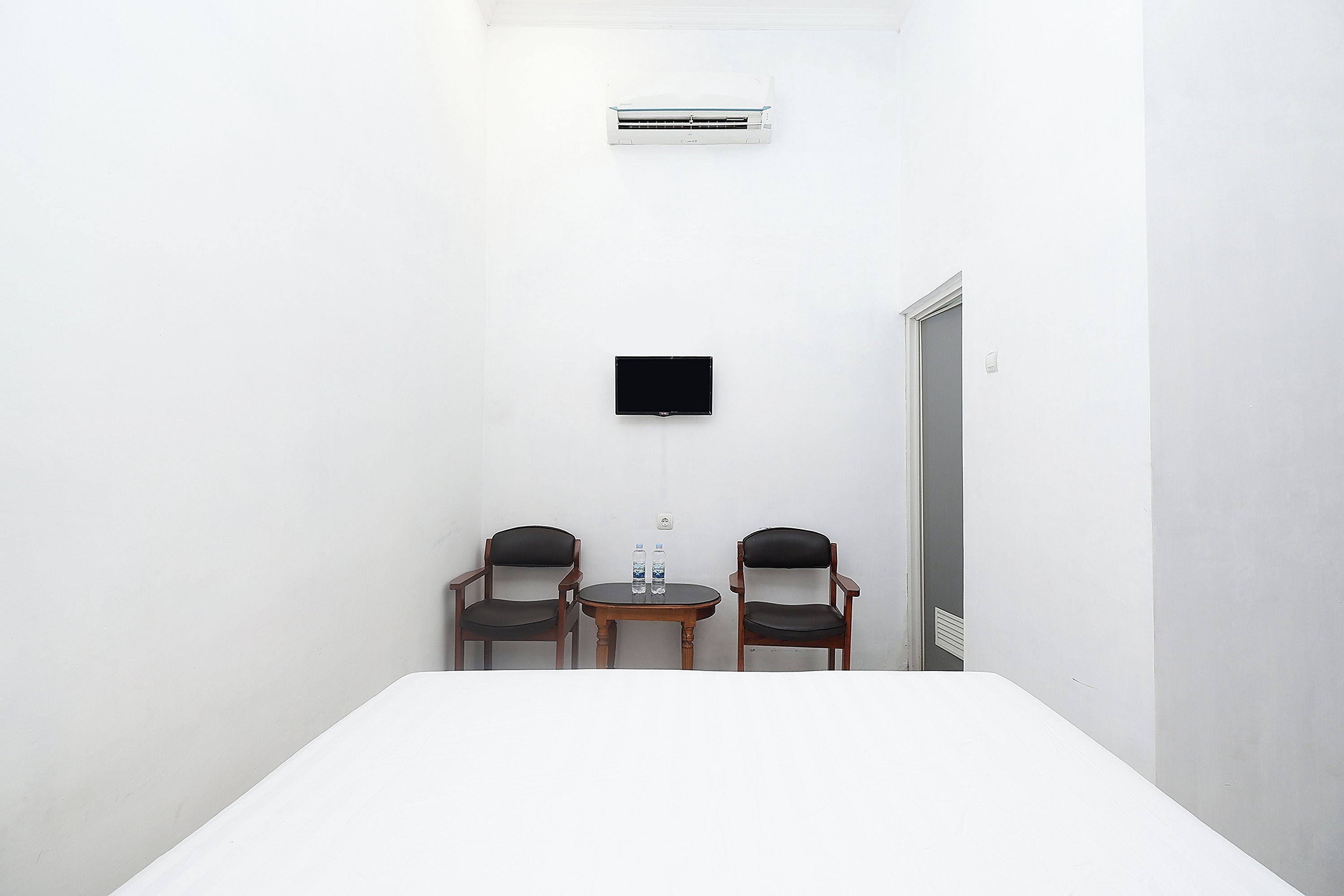 A small room with a white table, two chairs, a flat-screen TV, and an air conditioner.