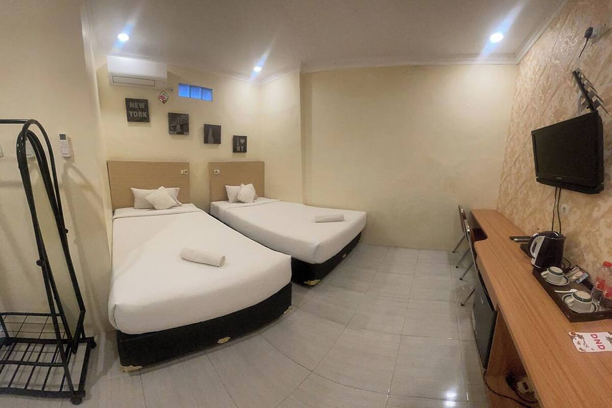 Ein Hotelzimmer mit zwei Betten, einem Schreibtisch mit Fernseher, einem kleinen Tisch und einem an der Wand montierten Fernseher.