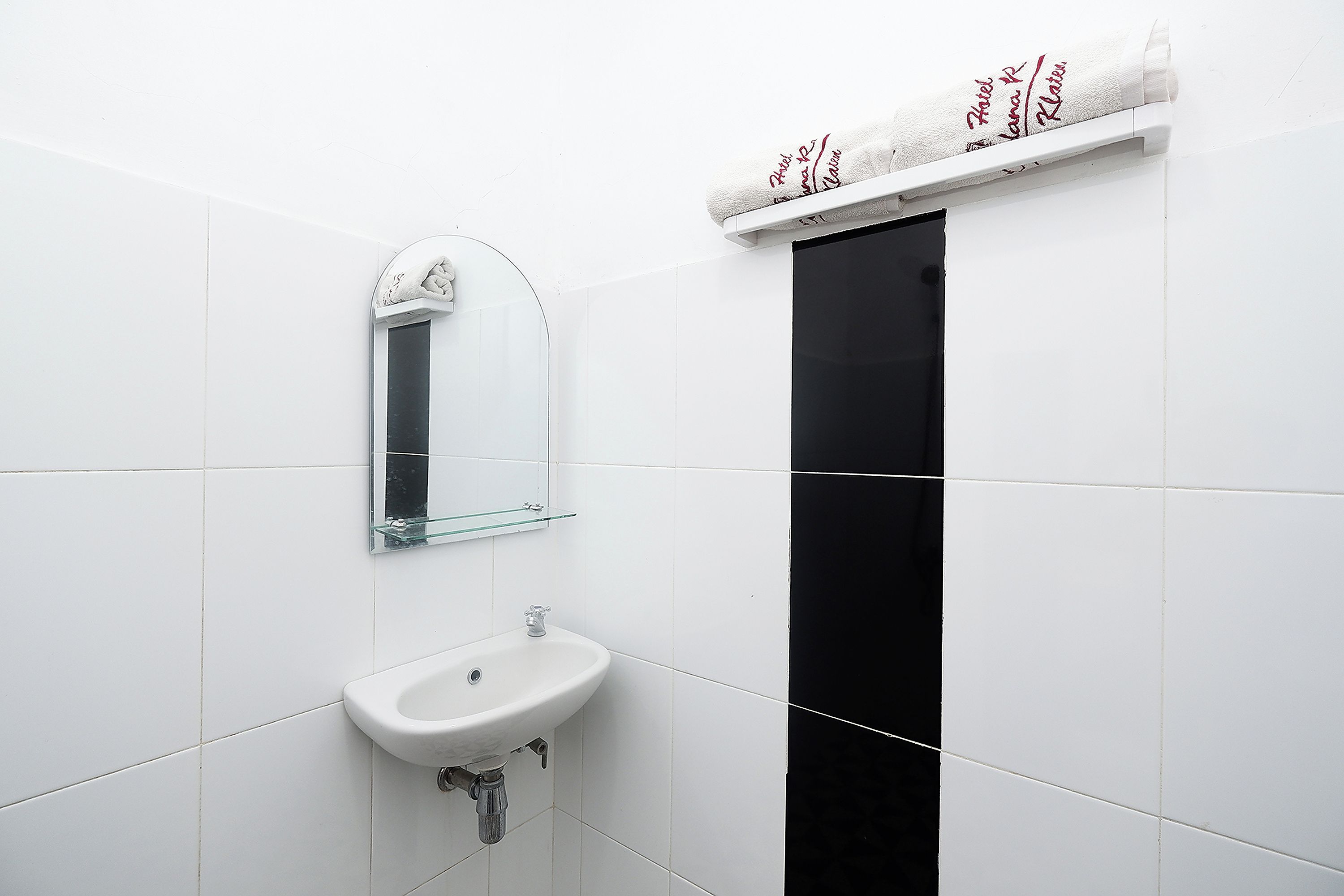 A bathroom with a white sink, a glass shelf, a mirror, and a towel rack with a towel.