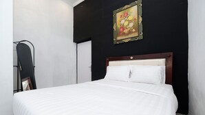 A bed with white bedding, a wooden headboard, and a painting of flowers on the wall. - Perdana Kasih Hotel Klaten by Zuzu (Klaten)