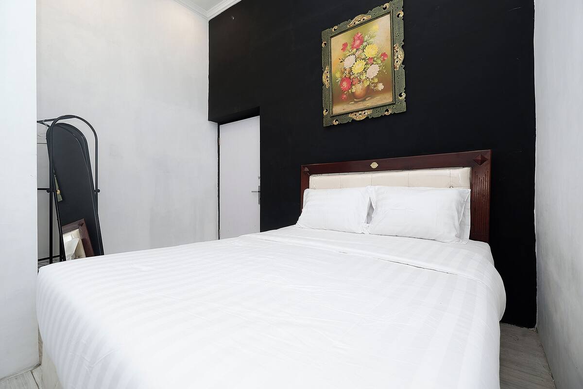 Ein Bett mit weißer Bettwäsche, einem Holzkopfst ück und einem Blumenbild an der Wand.