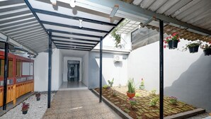 A covered outdoor area with a tiled floor, potted plants, and a pathway leading to a building entrance. - Perdana Kasih Hotel Klaten by Zuzu (Klaten)