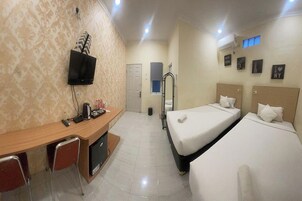 A hotel room with a desk, two beds, a TV, and a window.