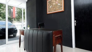 A room with a black leather sofa, a framed picture on the wall, a small table with a plant, and a door. - Perdana Kasih Hotel Klaten by Zuzu (Klaten)