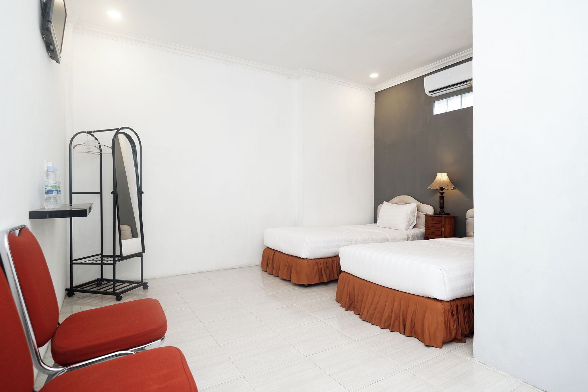 A hotel room with two beds, a desk, a chair, and a water bottle.
