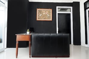 A black leather sofa, a wooden side table with a potted plant, and a framed picture on a black wall. - Perdana Kasih Hotel Klaten by Zuzu (Klaten)