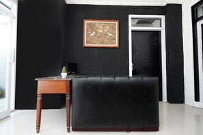Un canapé en cuir noir, une table d’appoint en bois avec un pot de plante et un tableau encadré sur un mur noir.
