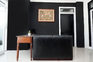 Um sofá de couro preto, uma mesa lateral de madeira com uma planta em vaso, e um quadro numa parede preta.
