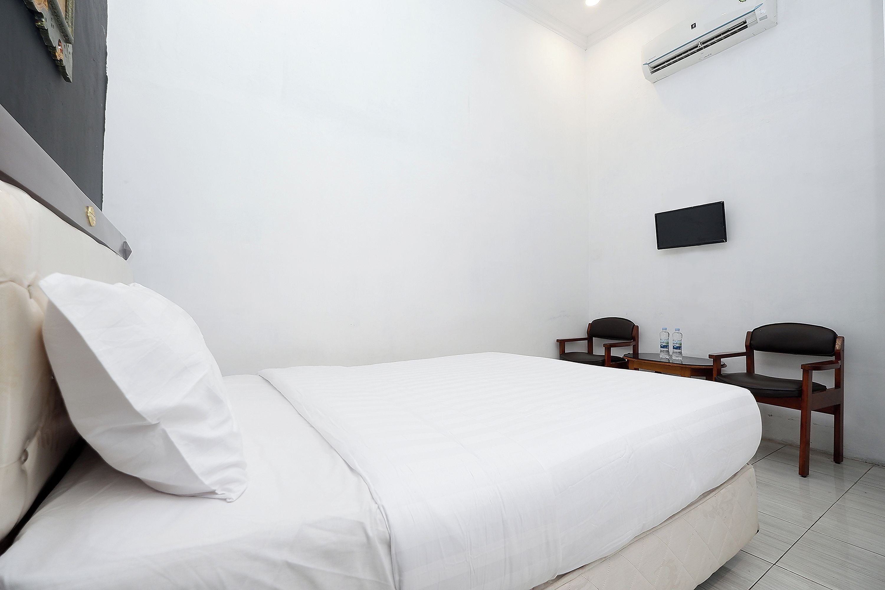 A hotel room with a bed, a TV mounted on the wall, and two chairs.