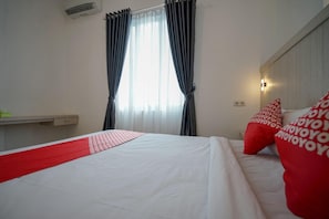 A hotel room with a bed, a window with curtains, a bedside table, and a wall-mounted light. - Max To U Hotel (Palembang)