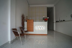 Una recepción con el nombre 'OYO' iluminado, dos sillas de mimbre, una planta decorativa y un suelo de baldosas.