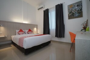 Habitación de hotel con cama, escritorio, silla, un cuadro y ventana con cortinas.