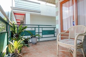 A balcony with potted plants, a wicker chair, and a door with a sign. - Spot On 2046 Villa Hardi (Batu)