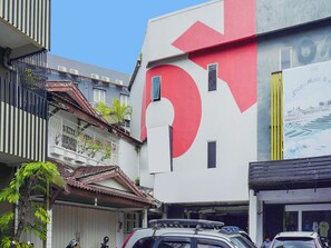 A building with a large red arrow sign, a balcony with plants, and a parked car. - Ht O Makassar Near Mall Panakukkang (Makassar)