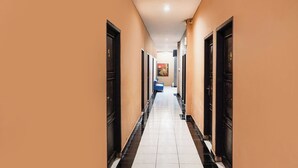 A hotel hallway with doors on both sides, a tiled floor, and a blue chair in the distance. - Ht O Makassar Near Mall Panakukkang (Makassar)