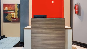 A reception desk with a modern design, a fire extinguisher mounted on the wall, and a piece of abstract art on the wall. - Ht O Makassar Near Mall Panakukkang (Makassar)