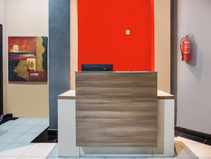 A reception desk with a modern design, a fire extinguisher mounted on the wall, and a piece of abstract art on the wall. - Ht O Makassar Near Mall Panakukkang (Makassar)