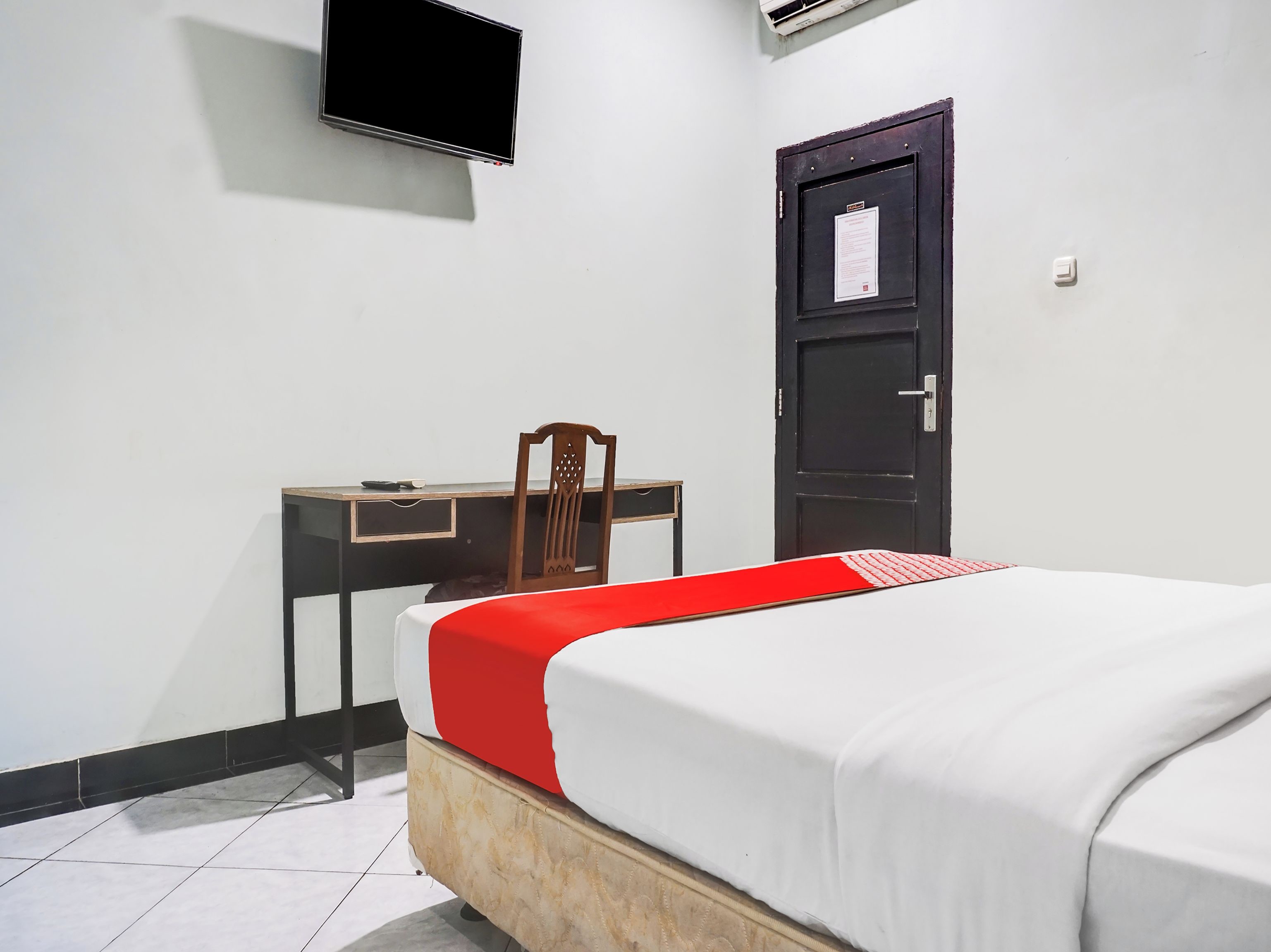 A room with a bed, a desk, a chair, a door, and a TV mounted on the wall.
