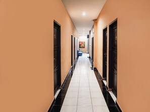 A hotel hallway with doors on both sides, a tiled floor, and a blue chair in the distance. - Ht O Makassar Near Mall Panakukkang (Makassar)