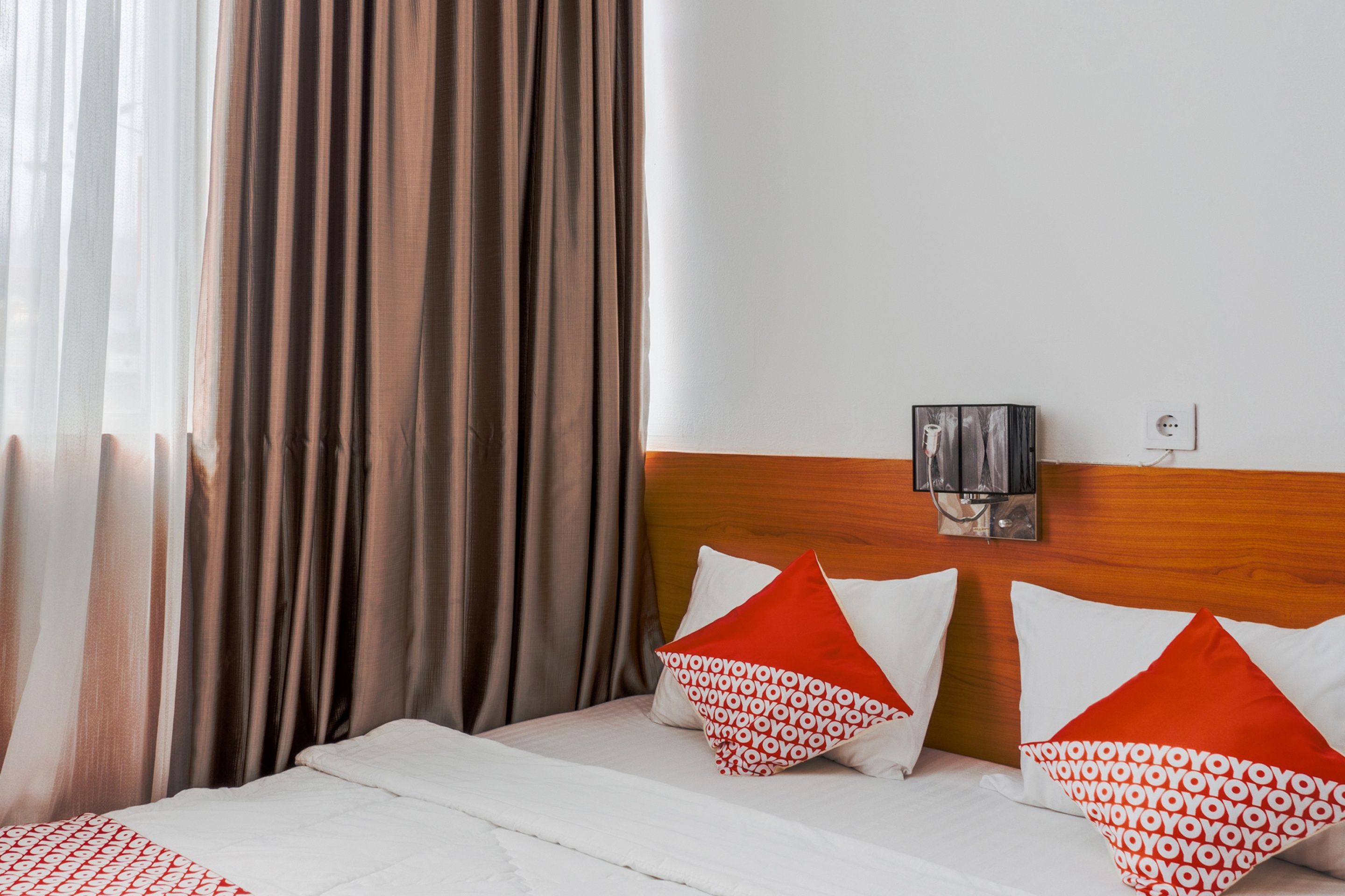 Ein Hotelzimmer mit einem Bett, Vorhängen, einer Wandleuchte und einem Holzkopfteil.