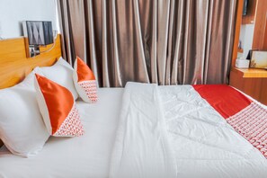 A hotel room with a bed, pillows, a headboard, curtains, and a bedside table with a lamp.