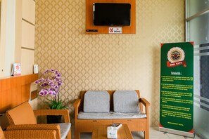 Un espace d’accueil comprenant un canapé, des fauteuils, un téléviseur, un panneau indiquant qu’il est interdit de fumer et un panneau indiquant qu’il s’agit de l’hôtel et de sa direction.