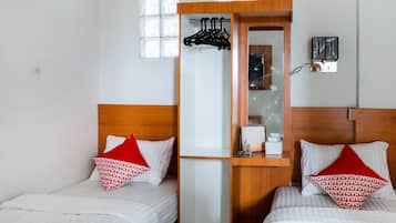 A hotel room with two beds, each with a red and white patterned pillow, a wooden headboard, and a small wooden desk with a mirror and a calendar.