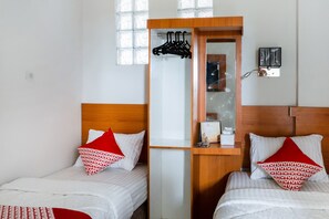 Une chambre d’hôtel avec deux lits, chacun agrémenté d’un oreiller à motifs rouges et blancs, d’une tête de lit en bois et d’un petit bureau en bois avec un miroir et un calendrier.