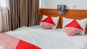 Una cama bien hecha con ropa de cama blanca y roja, dos almohadas con diseños blancos y rojos, y un cabecero de madera.