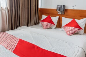 A neatly made bed with white and red bedding, two pillows with red and white patterns, and a wooden headboard.