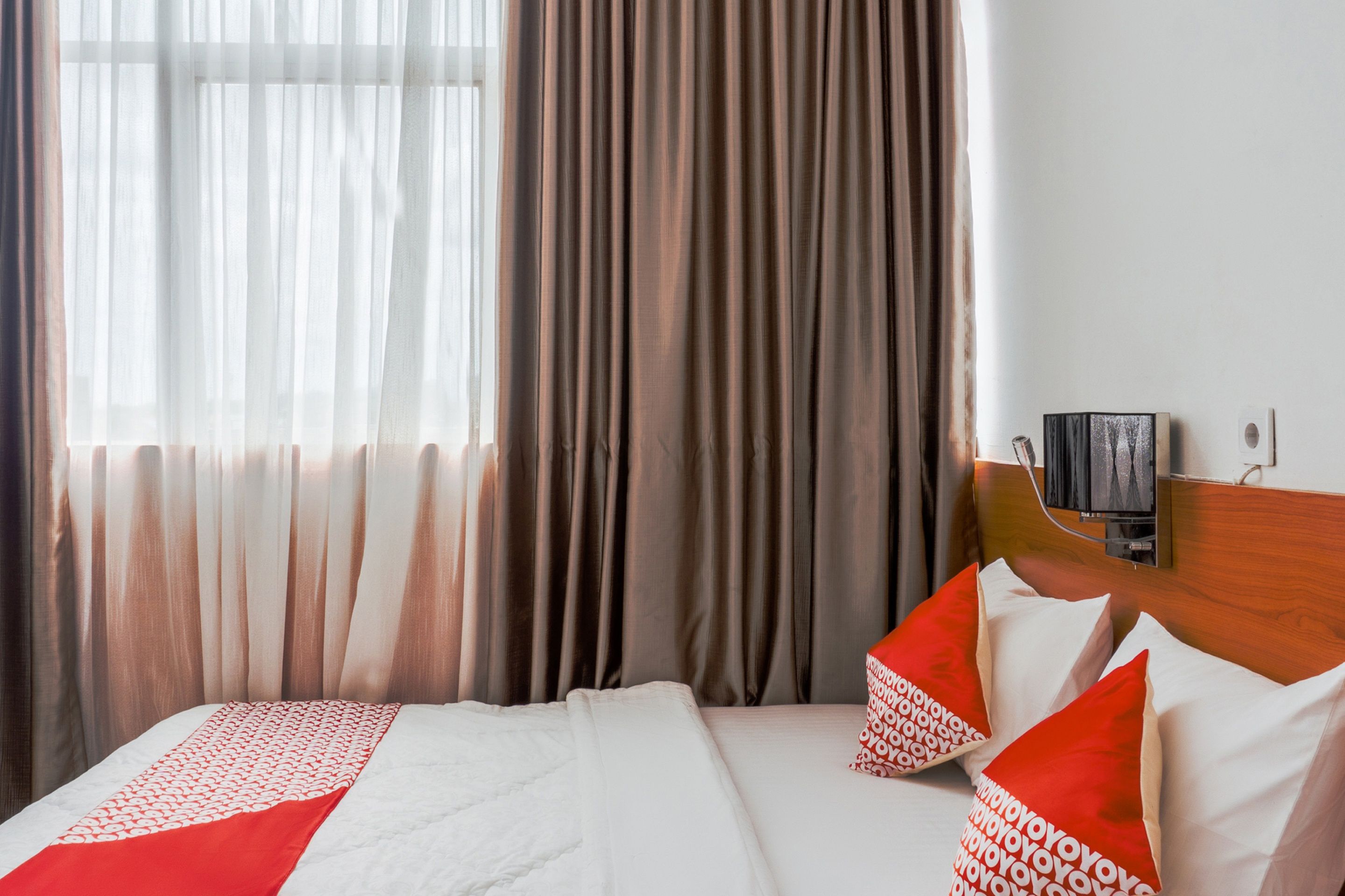 A hotel room with a bed, curtains, a television, and a wall-mounted TV.