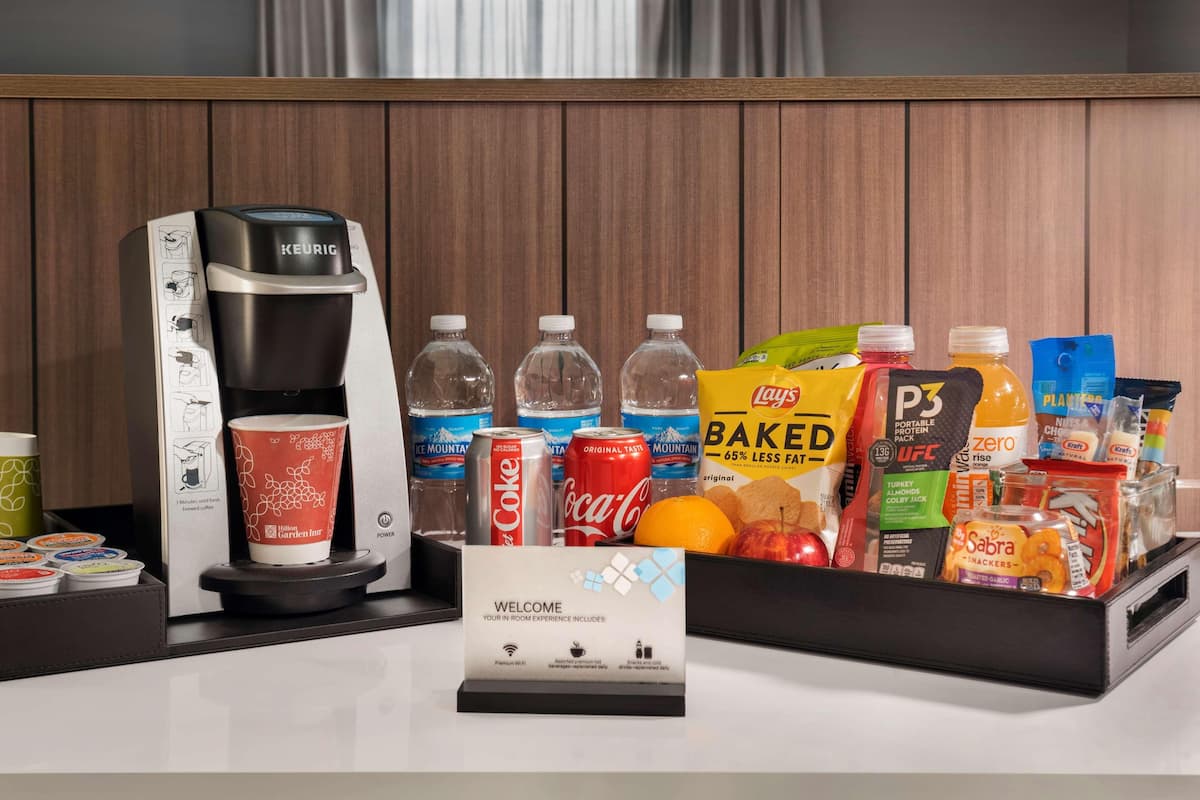 A hotel reception area with a Keurig coffee machine, various beverages, snacks, and a welcome sign.