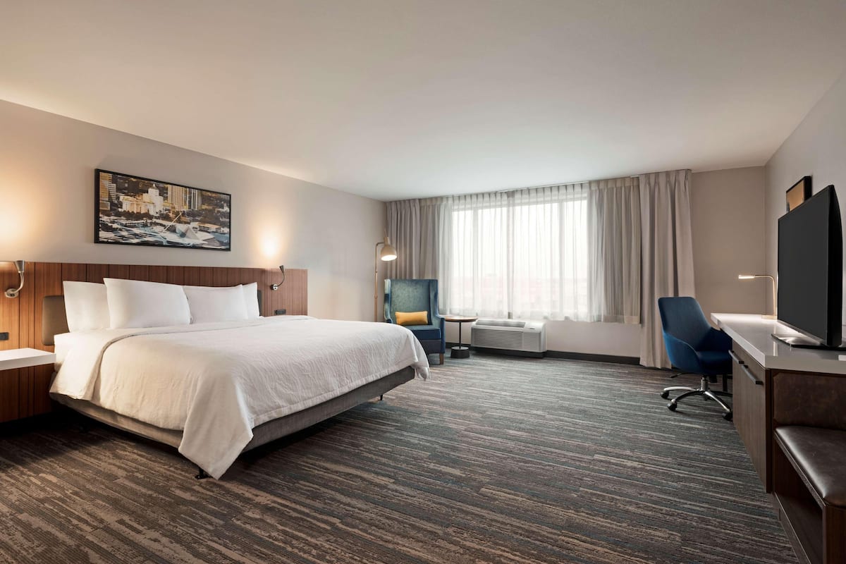 A hotel room with a large bed, a desk, a chair, a TV, and a painting on the wall.