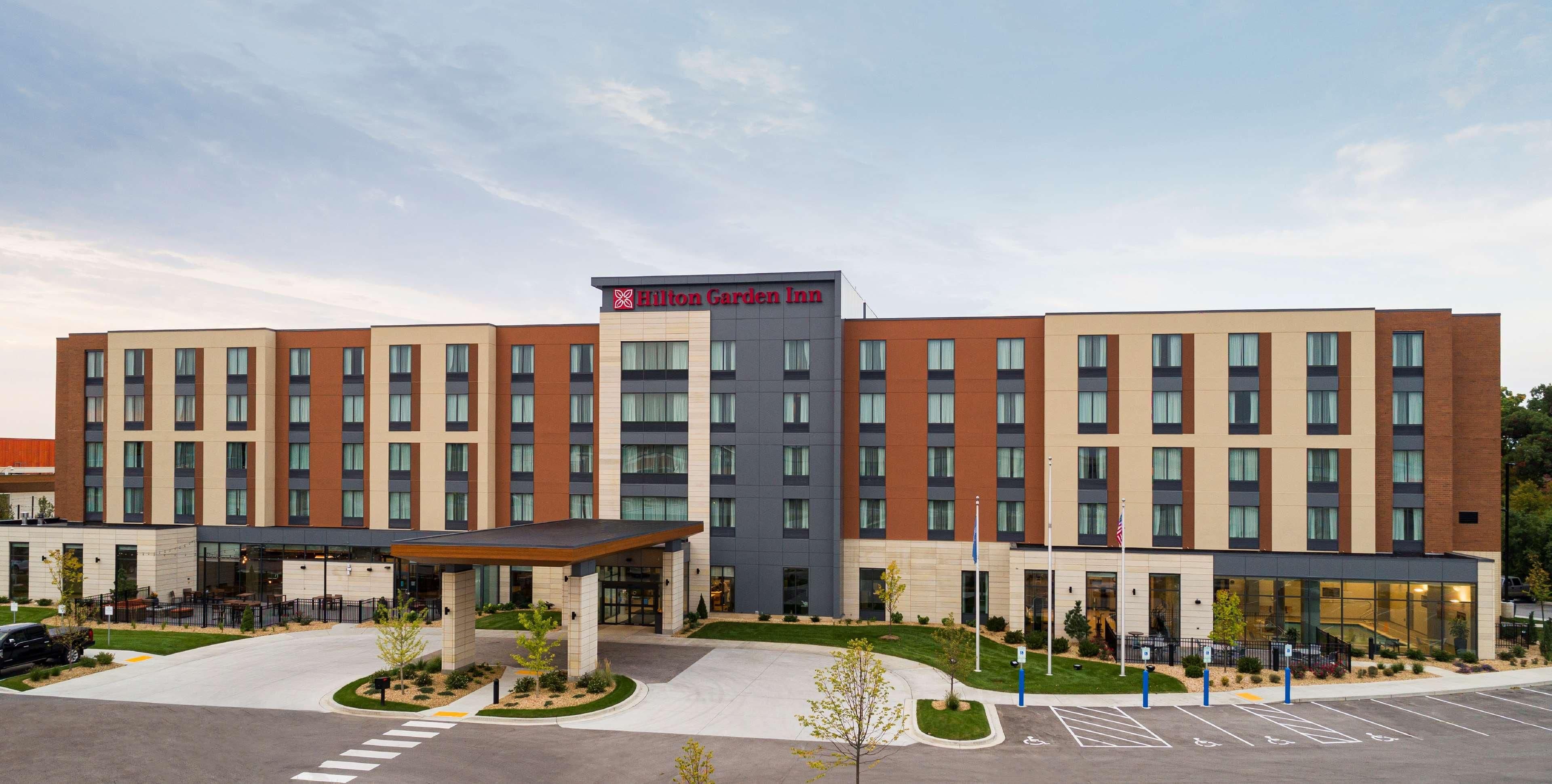 A multi-story hotel with a central entrance, a covered outdoor seating area, and a parking lot with handicapped spaces.