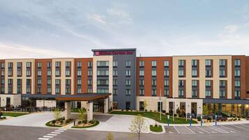 A multi-story hotel with a central entrance, a covered outdoor seating area, and a parking lot with handicapped spaces.
