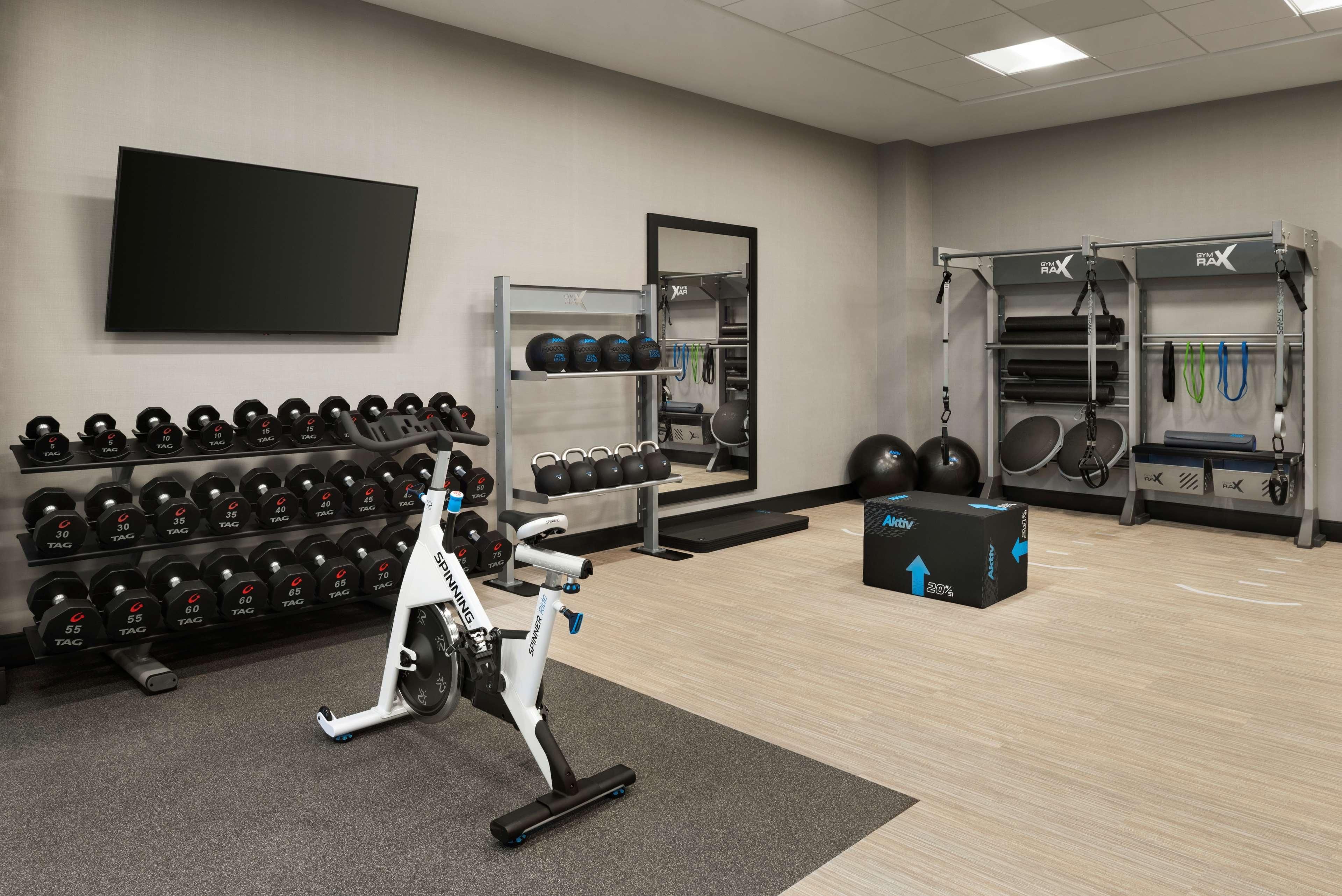 A gym with exercise equipment, a TV, and a wall-mounted rack of dumbbells.