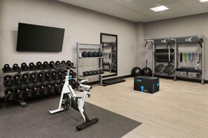 Ein Fitnessraum mit Trainingsgeräten, einem Fernseher und einem Wandboard für Kurzhanteln.