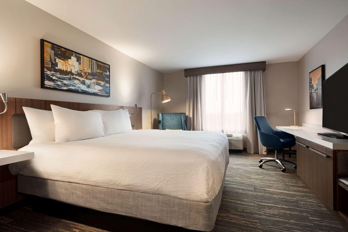 A hotel room with a large bed, a desk, a chair, a flat-screen TV, and a painting on the wall.