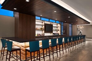 A modern bar area with a long counter, multiple bar stools, and a television screen.