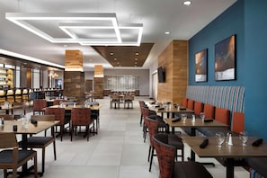 Un restaurante moderno con mesas y sillas de madera, una zona de bar y un espacio con bancos acolchados.