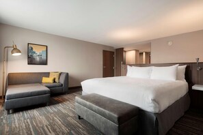 Una habitació d'hotel moderna amb un llit gran, un sofà, un petaca i un escriptori, i una làmpada.